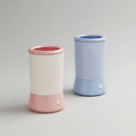 Two cylindrical containers, one pink and one blue, on a beige surface with a plain background.